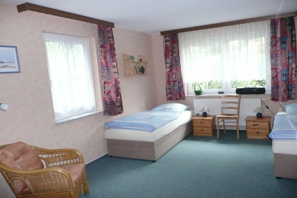 Een slaapkamer met een enkel bed, een stoel, een bureau en een raam met gordijnen.