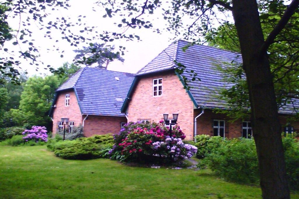 Een stenen huis met een schuin dak en een verzorgde tuin vol bloeiende planten.