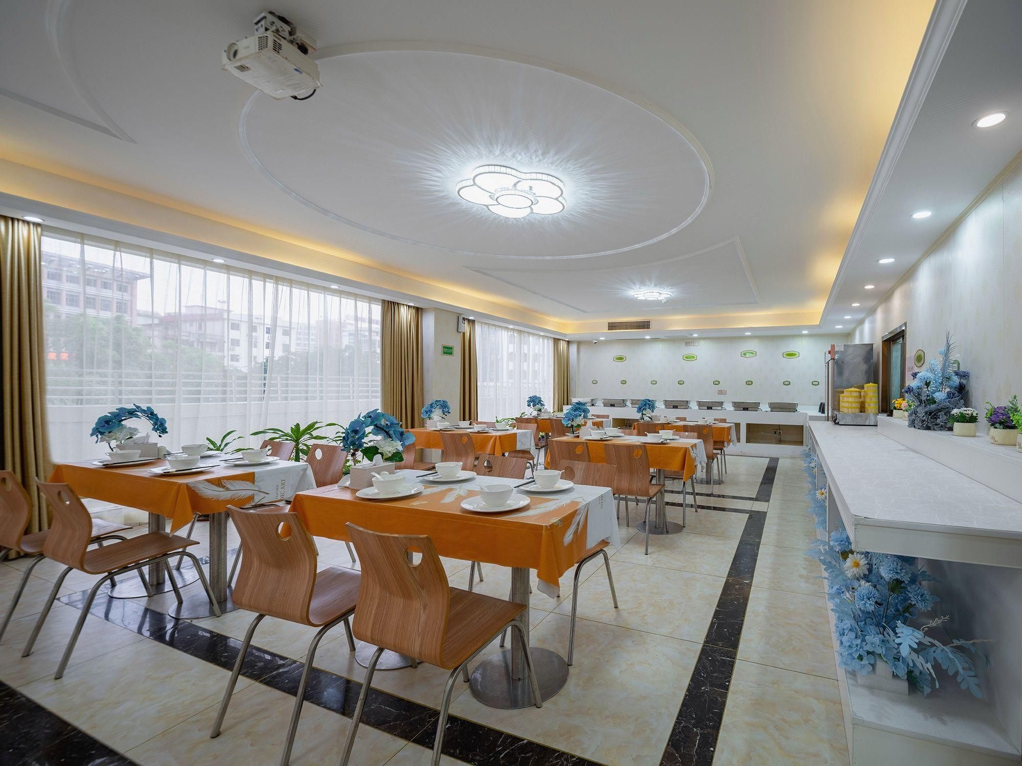A spacious dining area with multiple tables and chairs, a ceiling projector, and a view of buildings outside.