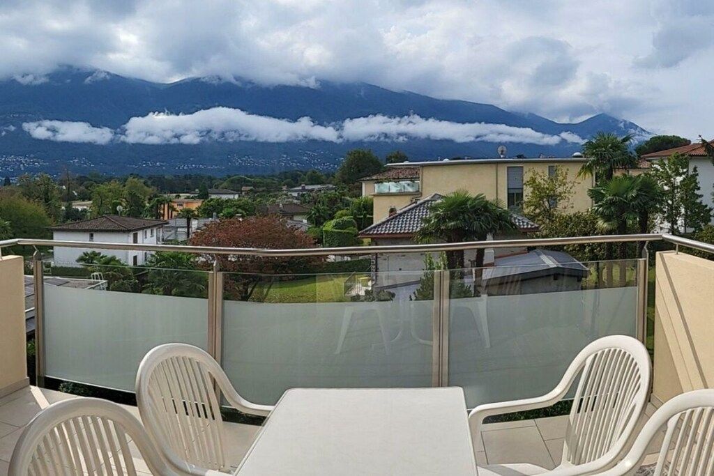 A balcony with a table and chairs, overlooking a residential area with houses and a mountain in the background.
