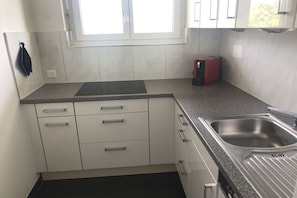 A compact kitchen with white cabinets, a granite countertop, a stainless steel sink, and a window above the sink. - Holiday apartment with 1 bedroom (Ascona)