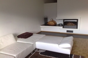 Ein modernes Wohnzimmer mit einem weißen Sofa, einem braunen Kissen, einem kleinen Tisch mit einem Korb und einem Kamin.