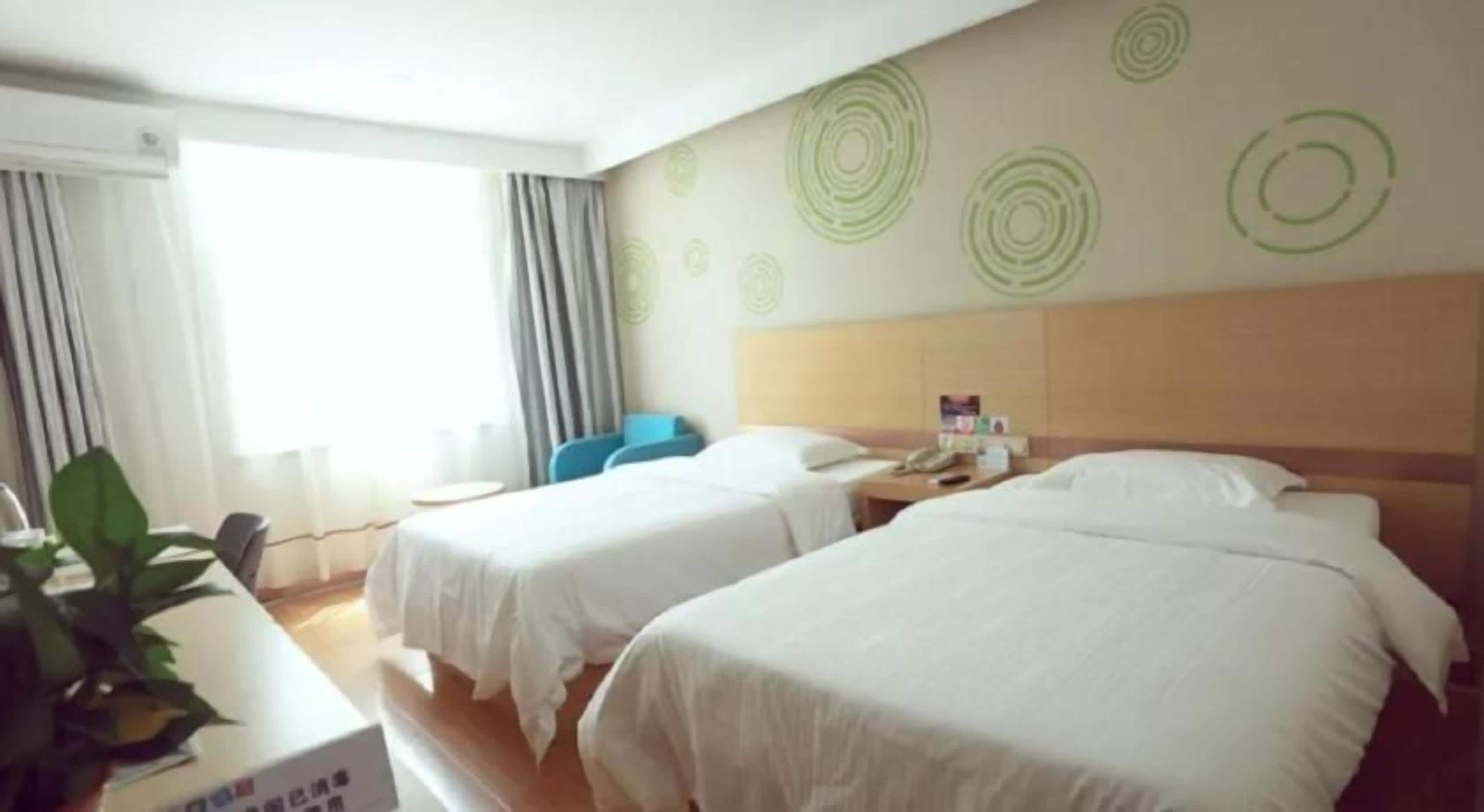 Une chambre d’hôtel avec deux lits, un bureau, une chaise et une fenêtre avec des rideaux.