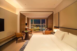 A hotel room with a large bed, a seating area with a table, and a view of a cityscape at night.