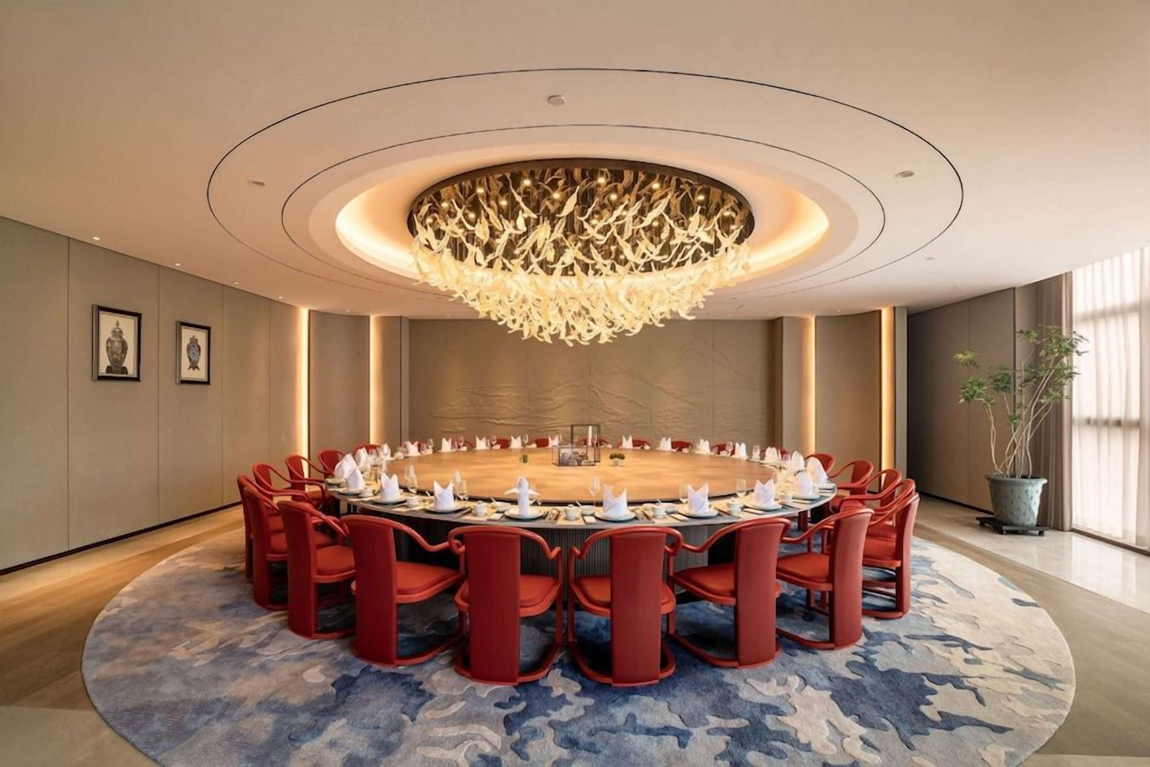 Een vergaderzaal met een ronde tafel, rode stoelen en een bijzondere kroonluchter.