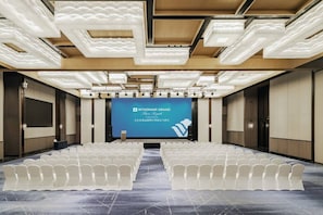A conference room with rows of chairs, a large screen, and a modern ceiling design.