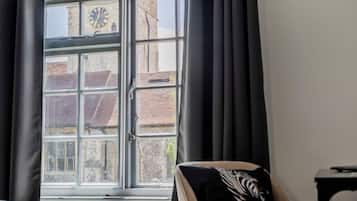 Una habitación con un ventanal grande, un reloj y una silla con un cojín a rayas.