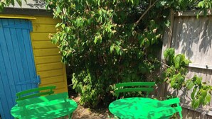 Dos sillas metálicas verdes y una mesa dispuestas al aire libre sobre una superficie pavimentada.