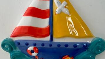 Ein dekoratives Segelboot mit einem gestreiften Segel, einem weißen Vogel und zwei Fischen.