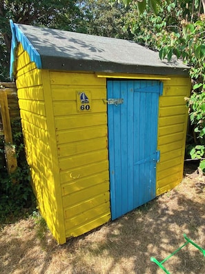 A small, single-story shed with a blue door and yellow siding, marked with the number 60. - Spacious coastal apartment with garden, sleeps 6 (West Sussex)