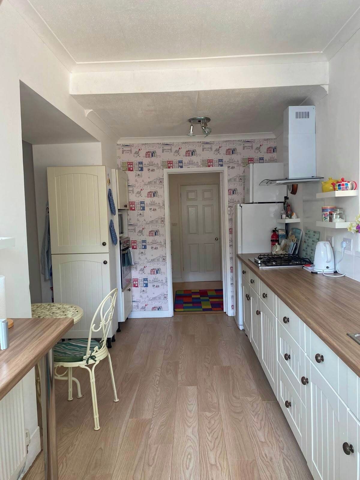 A narrow kitchen with a wooden countertop, a white refrigerator, and a colorful rug leading to a door.