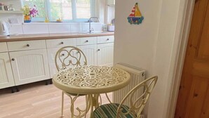 Un comedor con una mesa redonda y sillas, una cocina al fondo, y una puerta de madera.