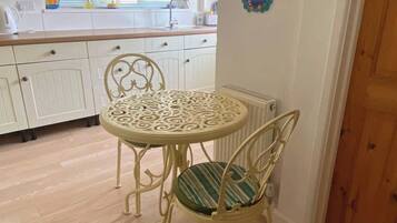 Un coin repas avec une table ronde et des chaises, une cuisine en arrière-plan et une porte en bois.