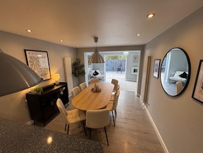 A modern dining area with a wooden table and chairs, a black console, and a large pendant light. - Lovely 5 bedroom holiday home with a games room (Christchurch)