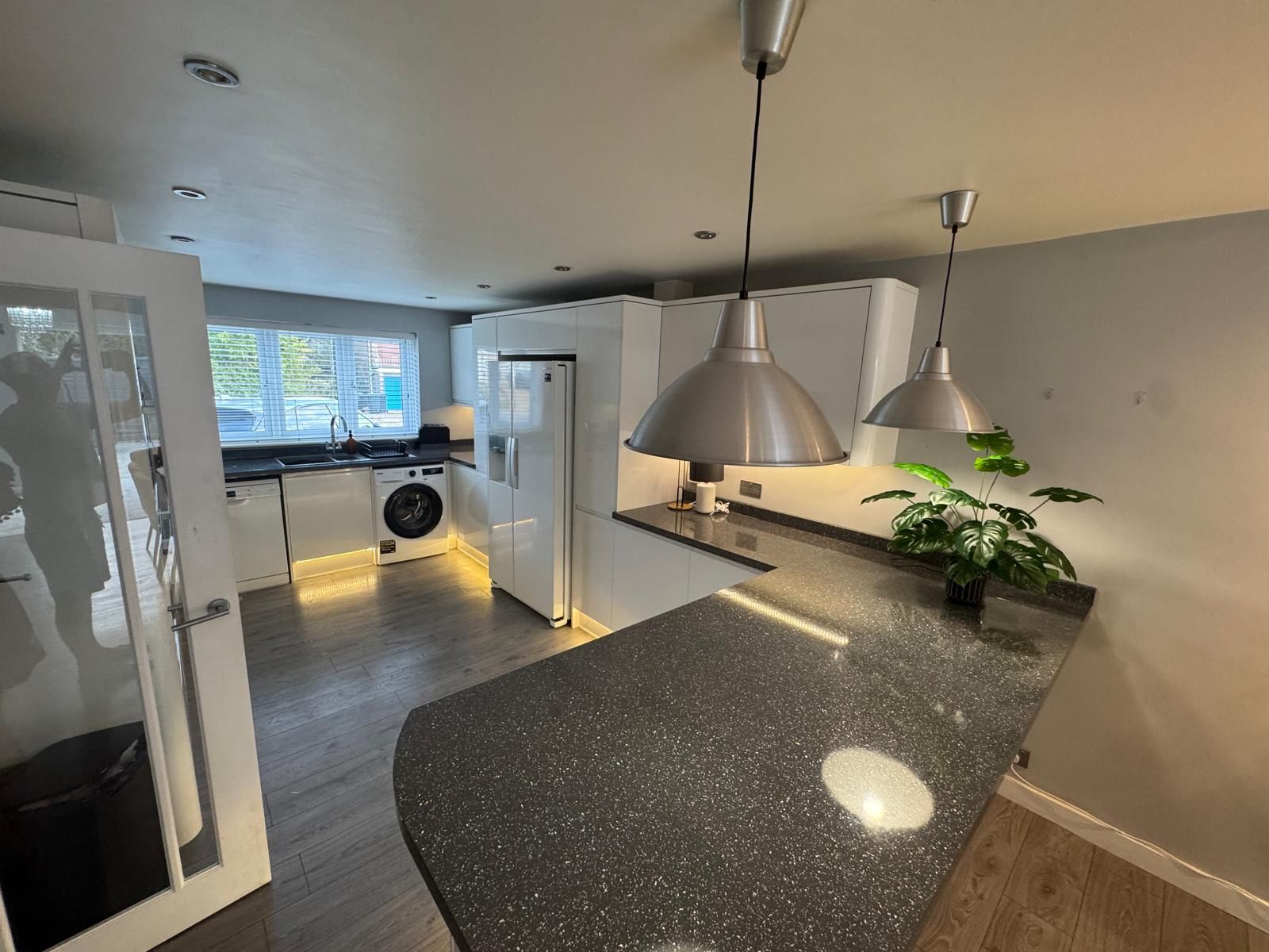 A modern kitchen with a granite countertop, stainless steel appliances, and pendant lighting.