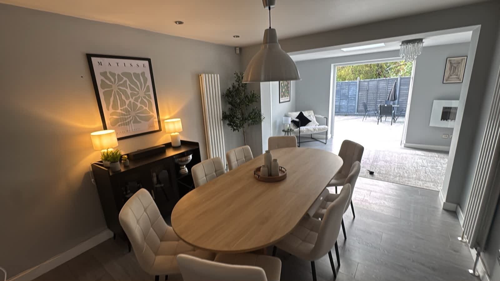 Et spiseområde med et rundt bord, stole, en hængende lampe og et billede i ramme på væggen.