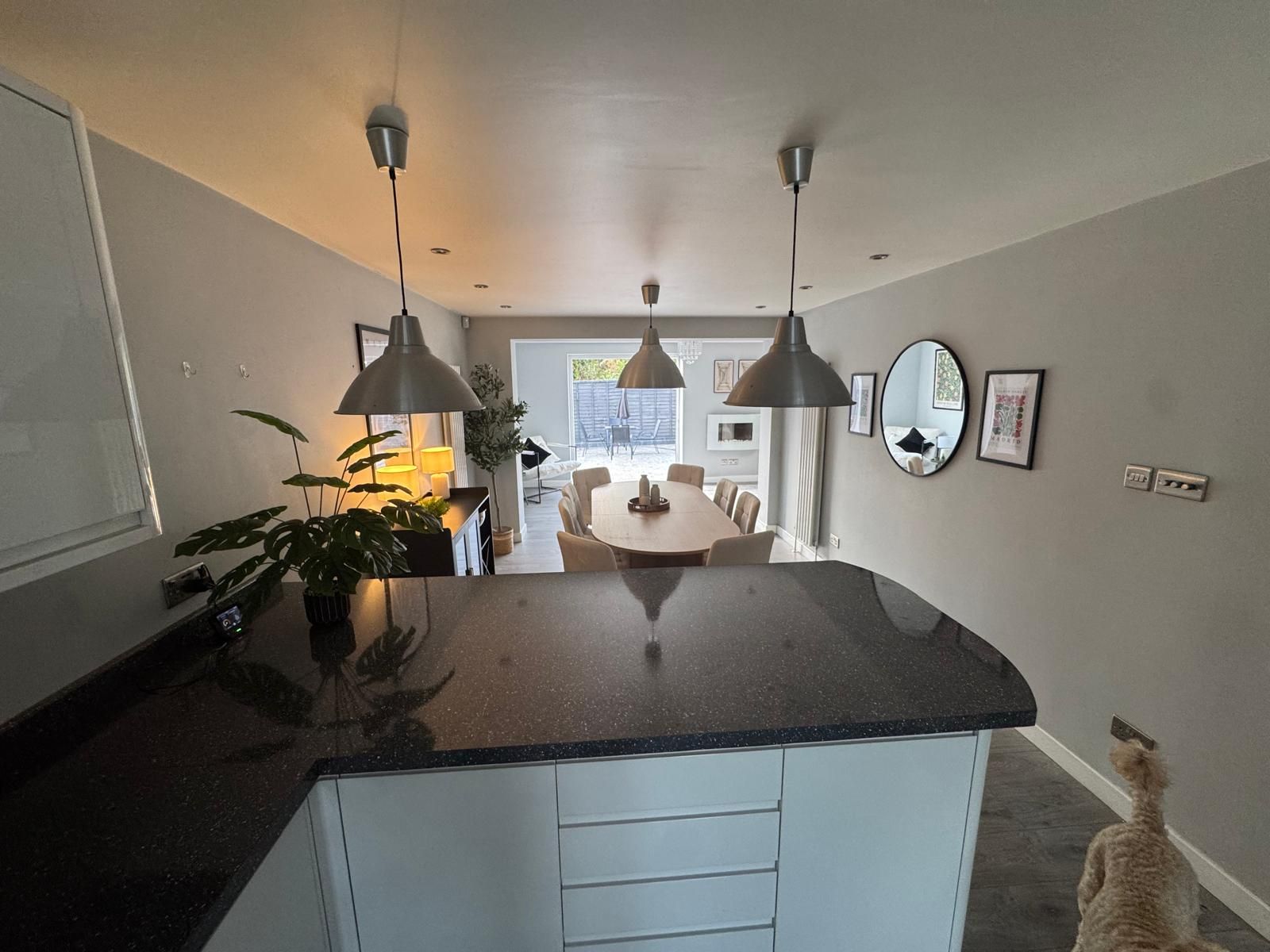 A modern kitchen with a central island, pendant lighting, and a dining area visible through an open door.
