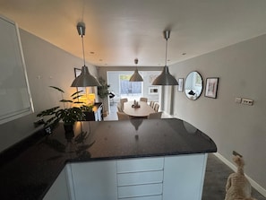 A modern kitchen with a central island, pendant lighting, and a dining area visible through an open door. - Lovely 5 bedroom holiday home with a games room (Christchurch)