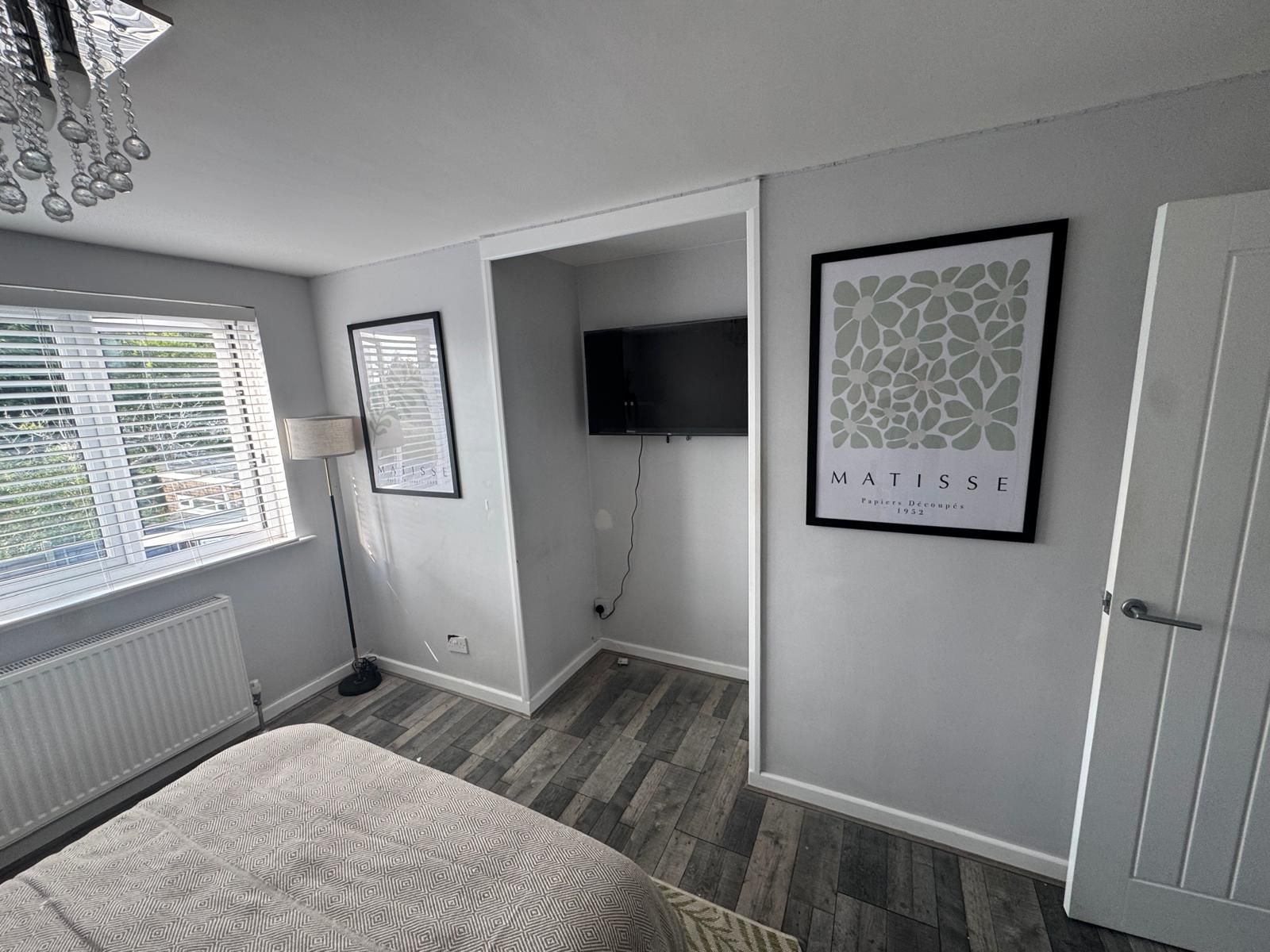 A bedroom with a bed, a TV, a framed artwork, and a radiator.