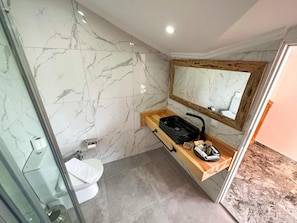 Un baño con pared de mármol, tocador de madera, lavabo y espejo.