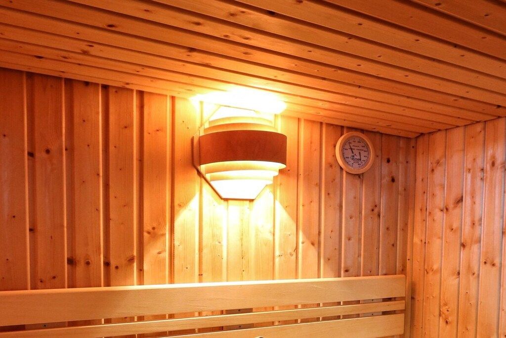 Uma sauna de madeira com um banco, uma luz fixada na parede e um relógio.
