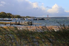 Ein Yachthafen mit vertäuten Booten, eine Holzsteganlage und ein Grünstreifen mit Schilf im Vordergrund.