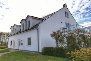Ein zweistöckiges Gebäude mit weißer Fassade, einem sichtbaren Eingang und einem Glasbalkon.