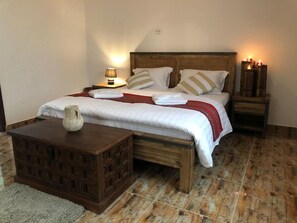Una cama bien hecha con almohadas, una lámpara de noche y un pequeño aparador de madera.