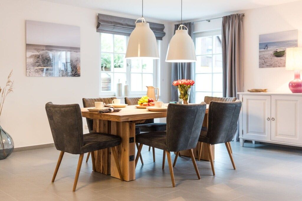 A dining area with a wooden table, six chairs, and pendant lights.