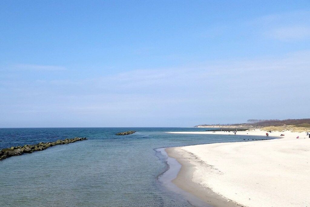 Ein Strand mit klarem Wasser, einem sandigen Ufer und einem steinernen Wellenbrecher.