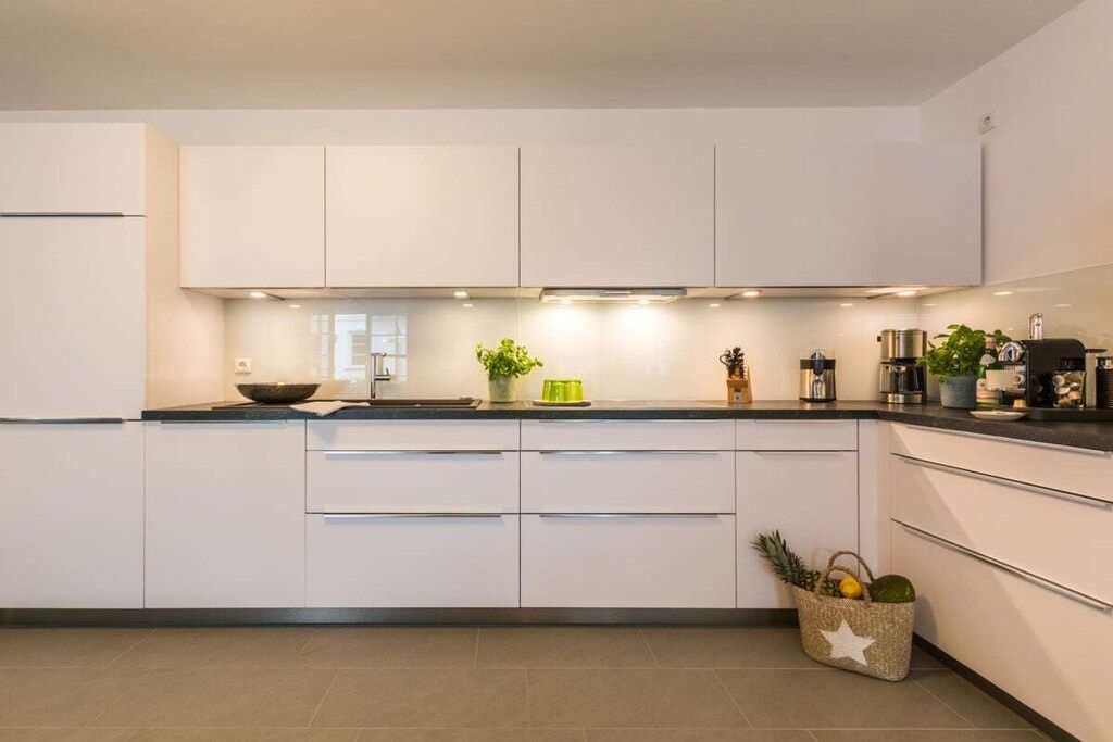 A modern kitchen with white cabinets, a black countertop, and a small plant on the counter.