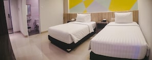 A hotel room with two beds, a bathroom with a toilet, and a wall with a geometric design. - Key Inn Hotel Bogor (Bogor)