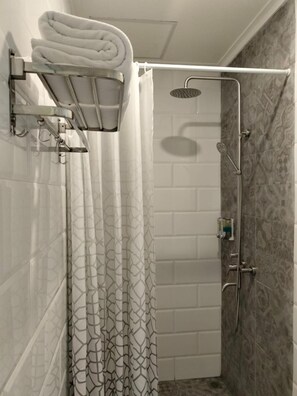 A shower area with a showerhead, a towel rack with folded towels, and a shower caddy. - Key Inn Hotel Bogor (Bogor)