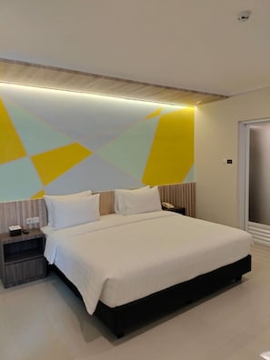A modern hotel room with a large bed, bedside tables, and a geometric wall design. - Key Inn Hotel Bogor (Bogor)