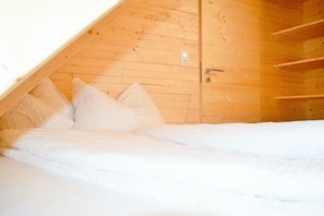 Une chambre avec un plafond en pente, des murs en bois, un lit avec une literie blanche et une porte dotée d’une poignée.
