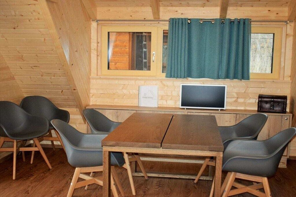 A wooden cabin with a dining area featuring a table and chairs, a television, and a window with curtains.
