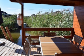 A wooden deck with a table and chairs, overlooking a body of water and dense vegetation.
