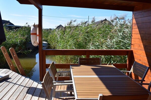 A wooden deck with a table and chairs, overlooking a body of water and dense vegetation.