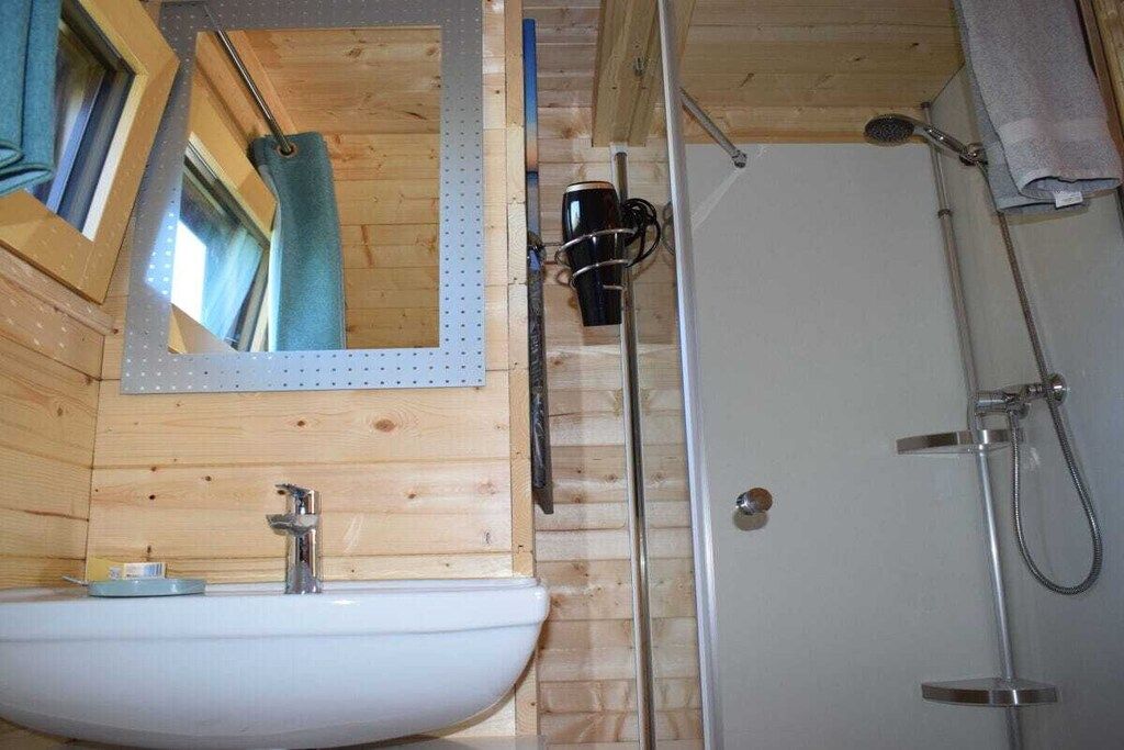 Ein Badezimmer mit Holzvertäfelung, einem weißen Waschbecken, einem Spiegel und einer Duschkabine.