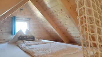 Ein gemütliches Schlafzimmer im Dachgeschoss mit schrägen Wänden, einem Bett mit weißer Decke und einem Fenster mit blauen Vorhängen.