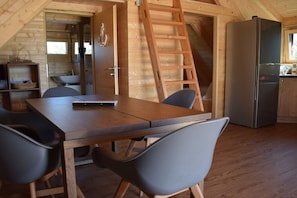 A wooden interior with a dining table, chairs, a refrigerator, and a wooden ladder.