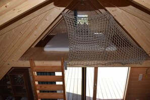 A wooden loft bedroom with a netted ceiling, a wooden ladder, and a window.