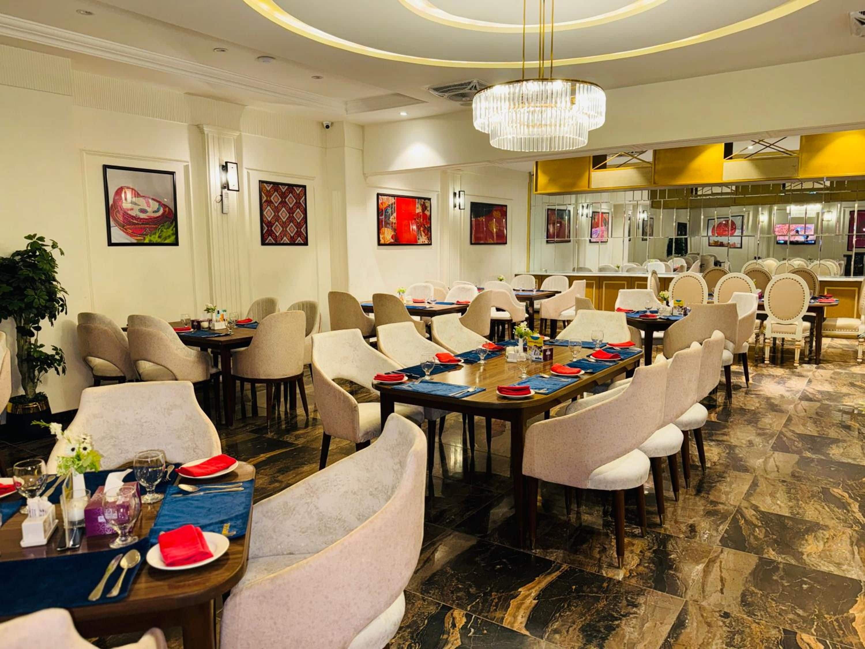 A hotel dining area with round tables, chairs, and a chandelier.
