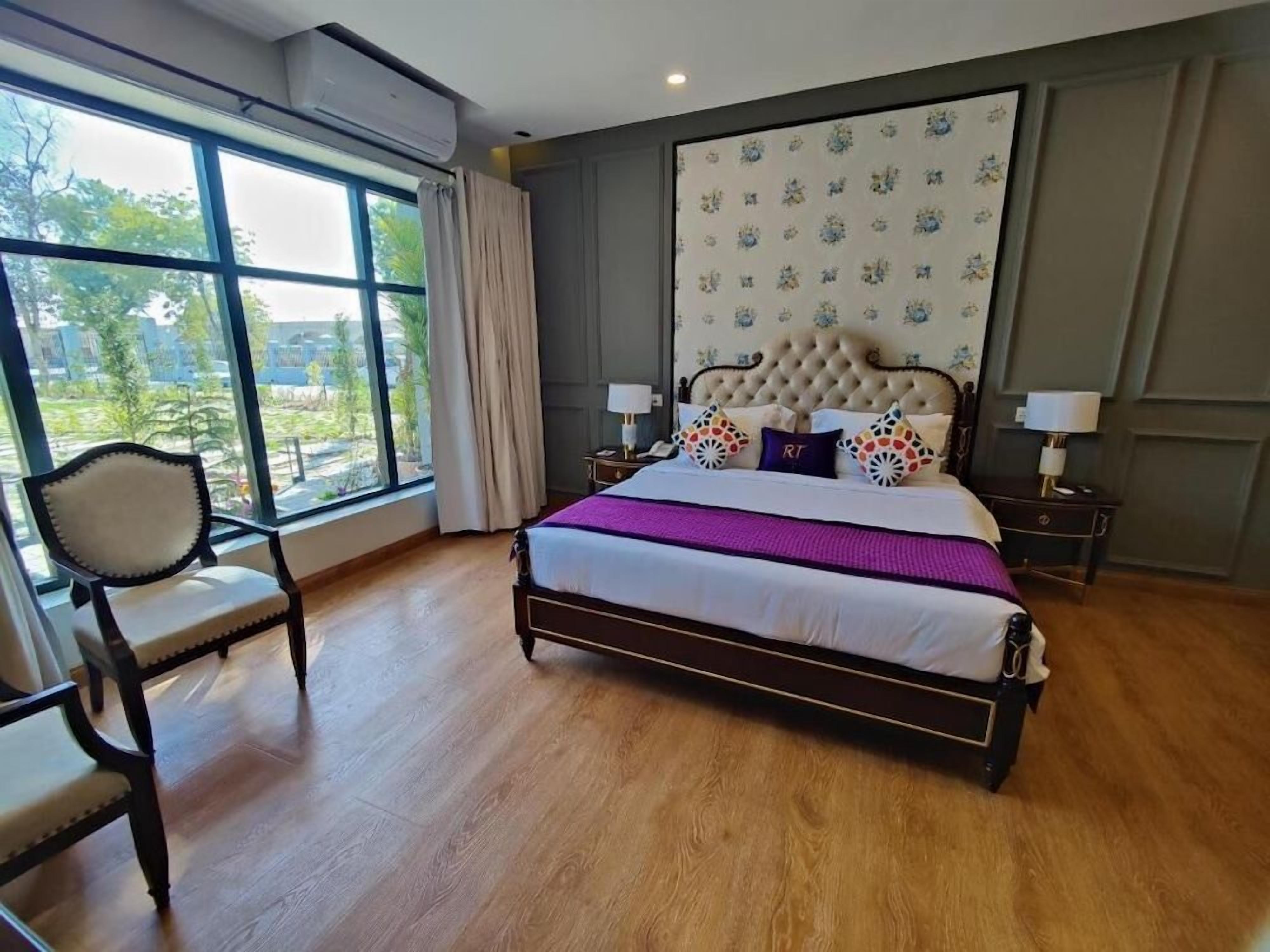 A bedroom with a large window, a bed with a tufted headboard, and a chair.