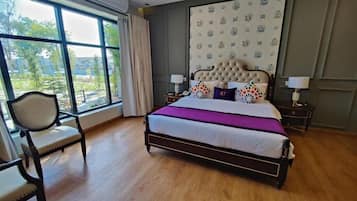 A bedroom with a large window, a bed with a tufted headboard, and a chair.