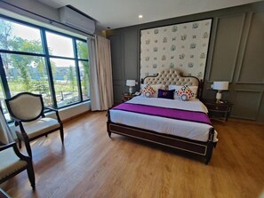 A bedroom with a large window, a bed with a tufted headboard, and a chair.
