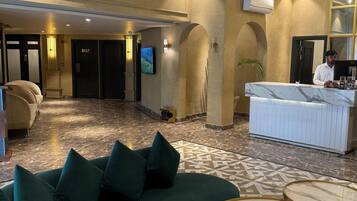 Um saguão de hotel com balcão de recepção, um sofá verde, piso de mármore e um espelho grande.
