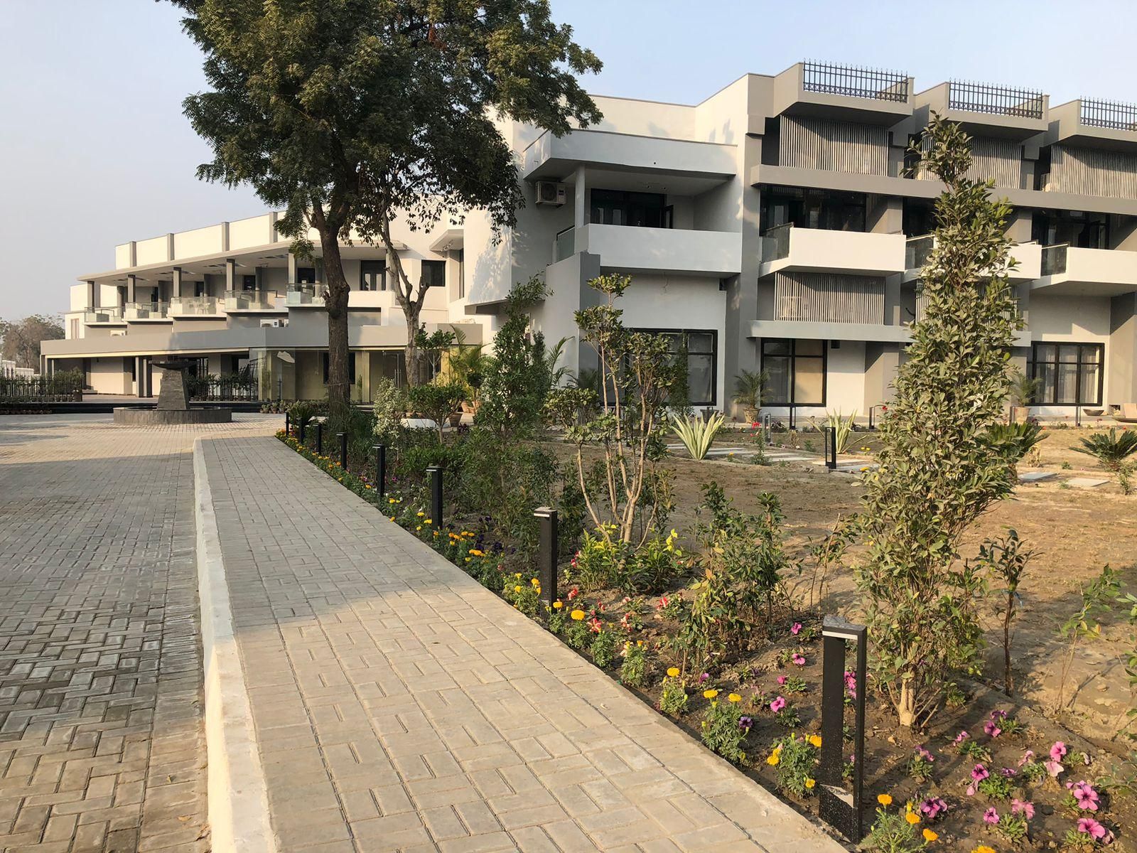 A modern building with multiple floors, a paved walkway, and landscaped areas with various plants and flowers.