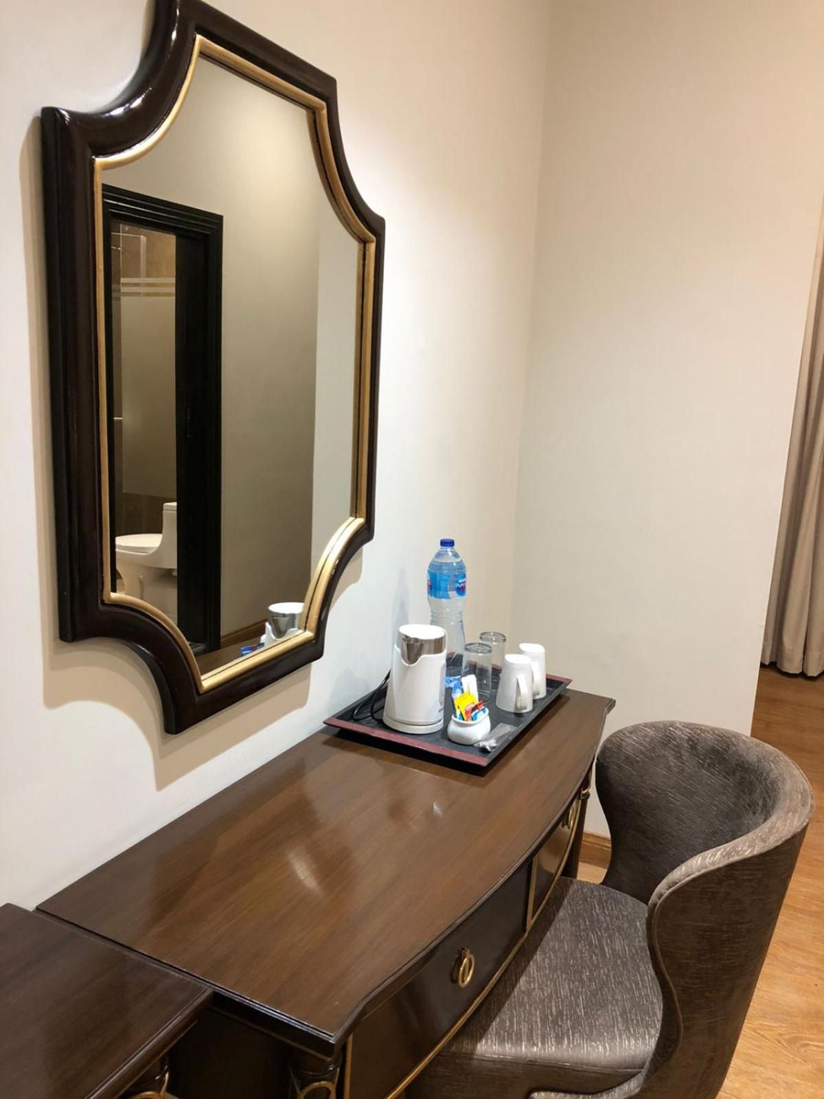 Ein Hotelzimmer mit Schreibtisch aus Holz, einem Sessel, einem großen Spiegel und einem Tablett mit Toilettenartikeln.