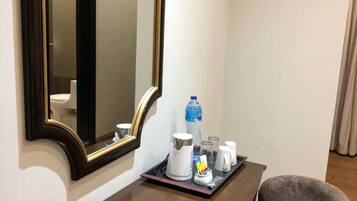 A hotel room with a wooden desk, a chair, a large mirror, and a tray with toiletries.